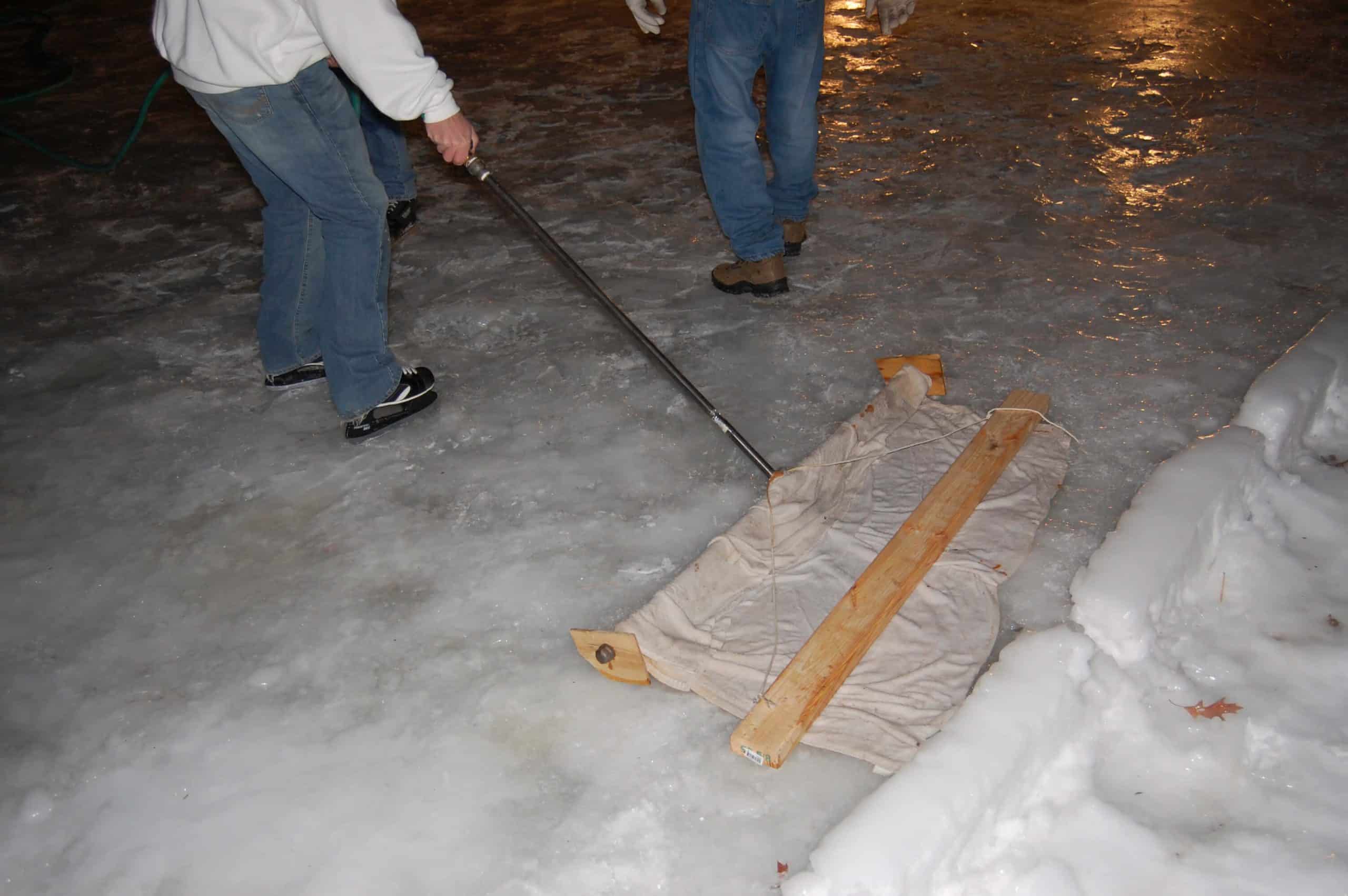 Two people performing maintenance on a DIY rink to keep it in perfect condition